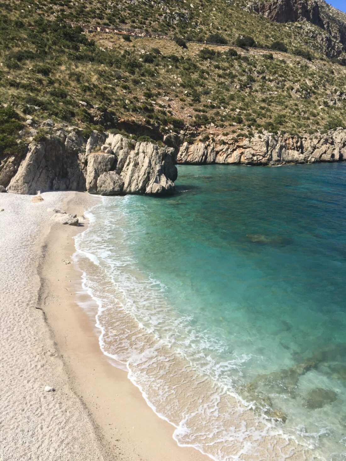 Skrytá malá pláž s bílým pískem a tyrkysovou vodou obklopená skalami v přírodním parku Zingaro na Sicílii