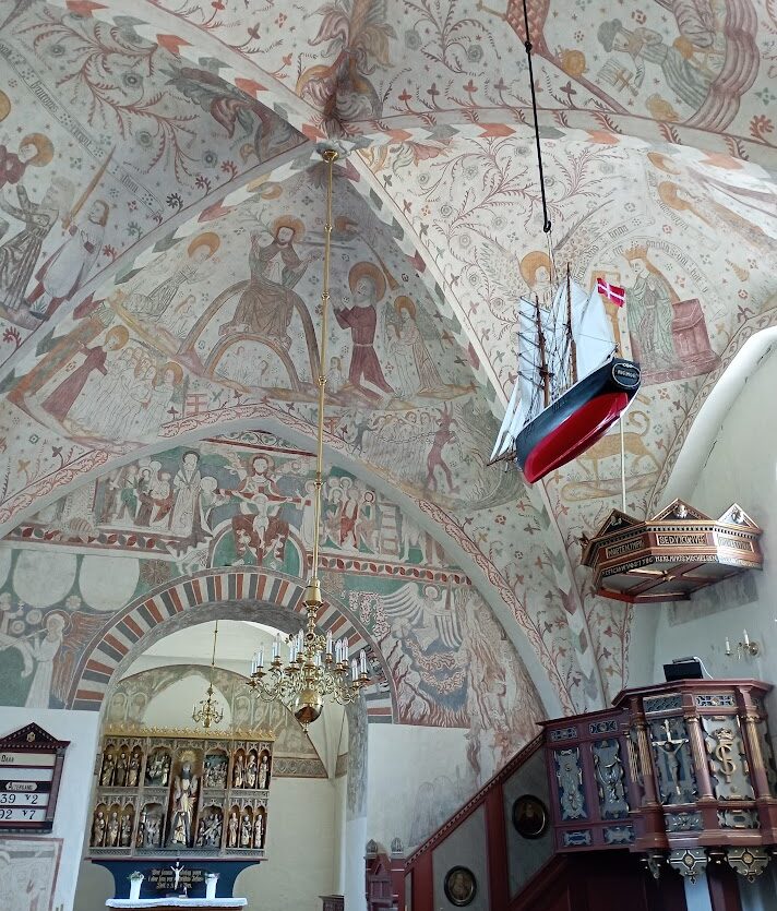 Fresky a plachtenice v kostele na ostrově Møn, zobrazení biblických příběhů a námořní historie na stěnách středověké dánské památky.